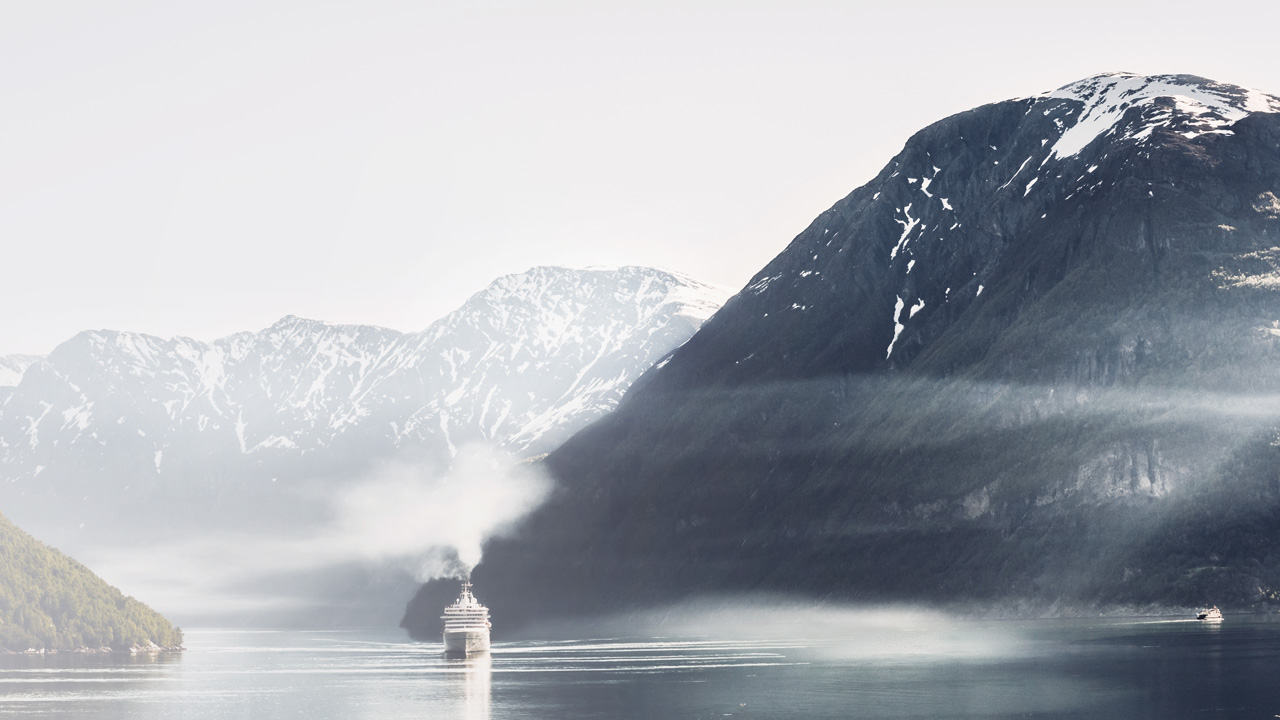 Cruise skip i norsk fjord, omringet av snøkledde fjell. 