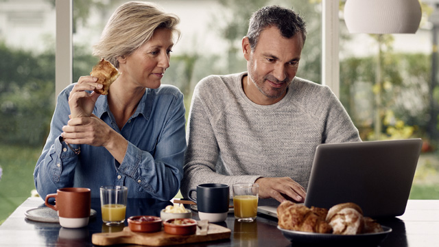 Couple home smiling eating with laptop - small